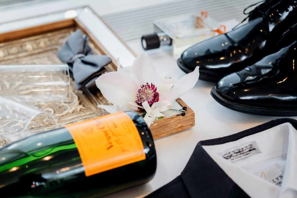 Flatlay with mens dress shoes, champagne, bowtie, cologne and boutonniere | Weddings & Events by Cheryl Munro | Toronto Wedding Planner