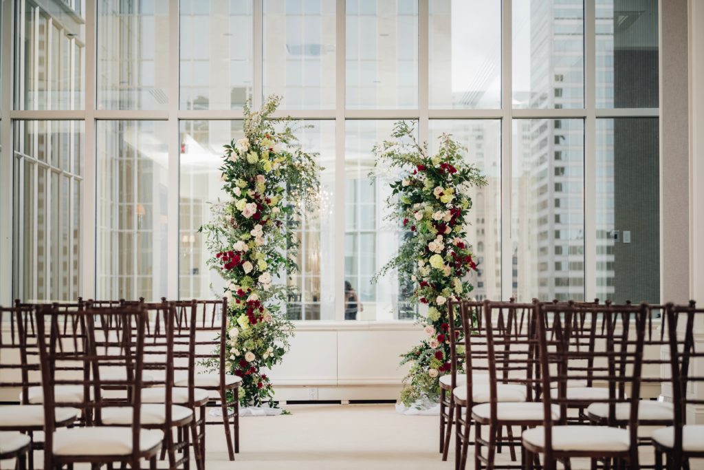 Dark wood chair down an aisle with a floral arch that has white, cream and burgundy flowers | Weddings & Events by Cheryl Munro | Toronto Wedding Planner