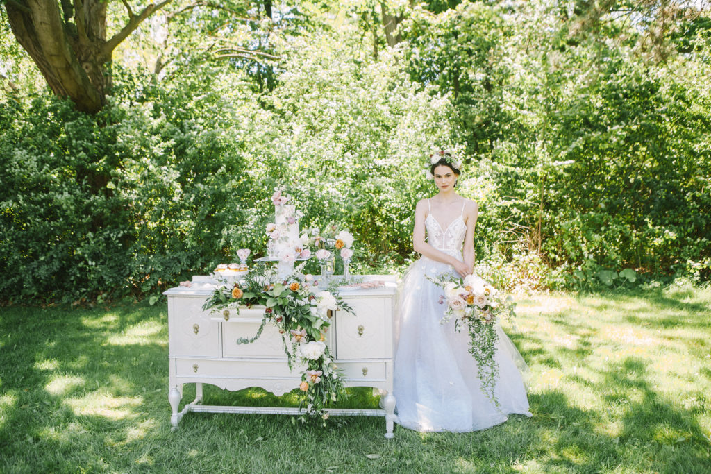Bride holding bouquet standing beside dessert table  | Weddings & Events by Cheryl Munro | Toronto Wedding Planner