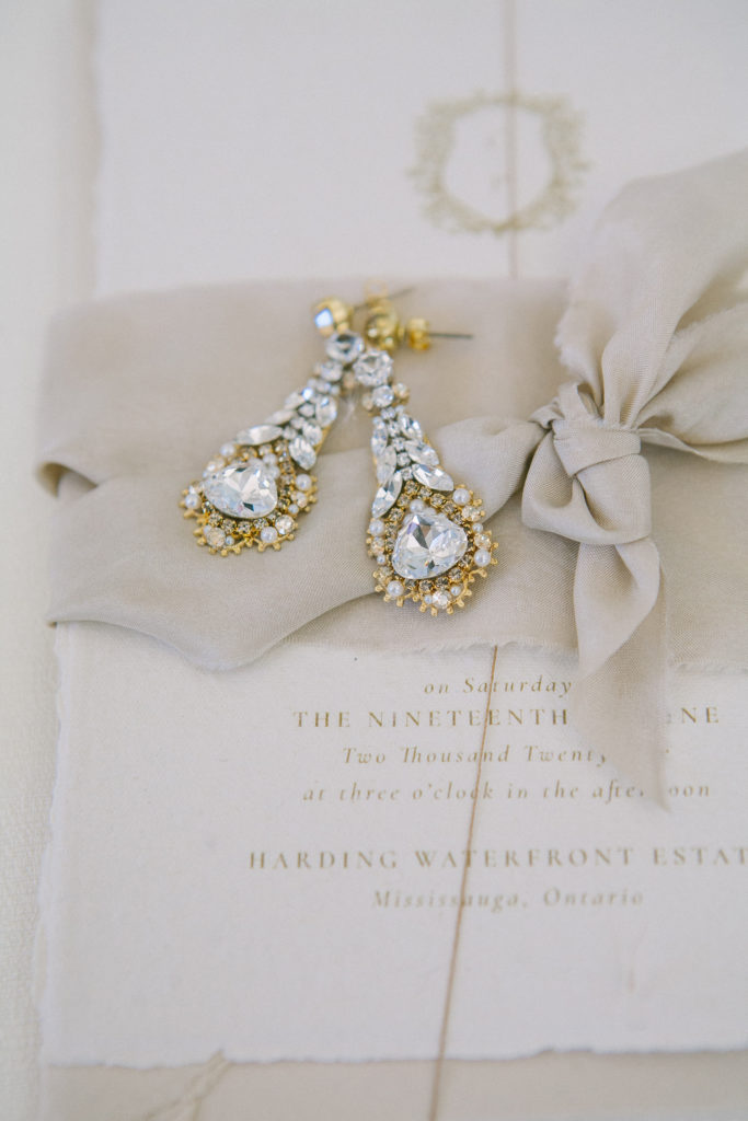 Gold and diamond earrings on nude wedding invitation with ribbon  | Weddings & Events by Cheryl Munro | Toronto Wedding Planner