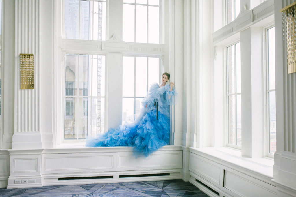 Bride in blue ruffle dress standing in large white floor to ceiling windows  | Weddings & Events by Cheryl Munro | Toronto Wedding Planner