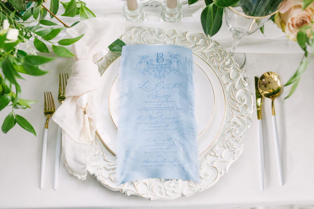 Table with a vintage white charger plate with a blue fabric menu and gold cutlery  | Weddings & Events by Cheryl Munro | Toronto Wedding Planner