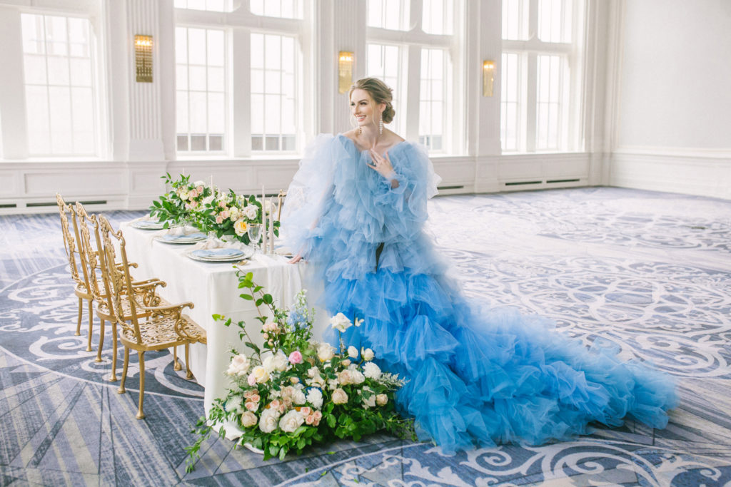 Bride in blue ruffle dress standing in front of a table with flowers and vintage gold chairs  | Weddings & Events by Cheryl Munro | Toronto Wedding Planner
