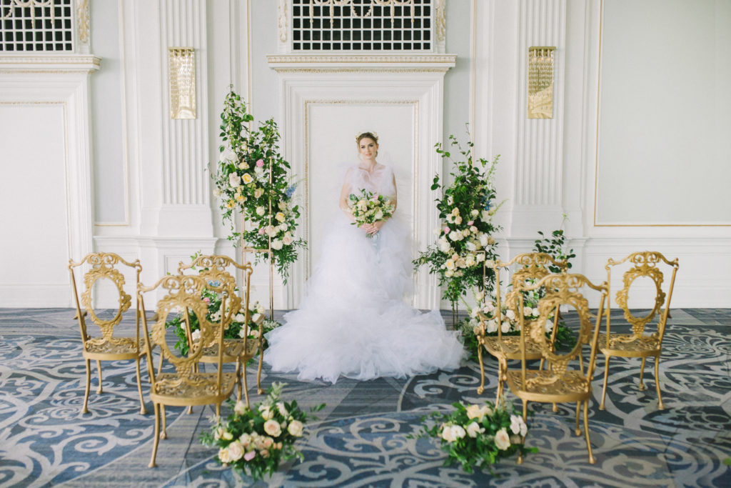 Bride in white ruffle wedding dress standing at floral alter with gold vintage ceremony chairs  | Weddings & Events by Cheryl Munro | Toronto Wedding Planner