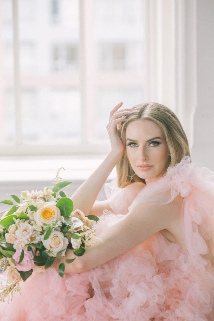 Bride in pink ruffle dress holding head in hand and holding a bouquet of flowers  | Weddings & Events by Cheryl Munro | Toronto Wedding Planner