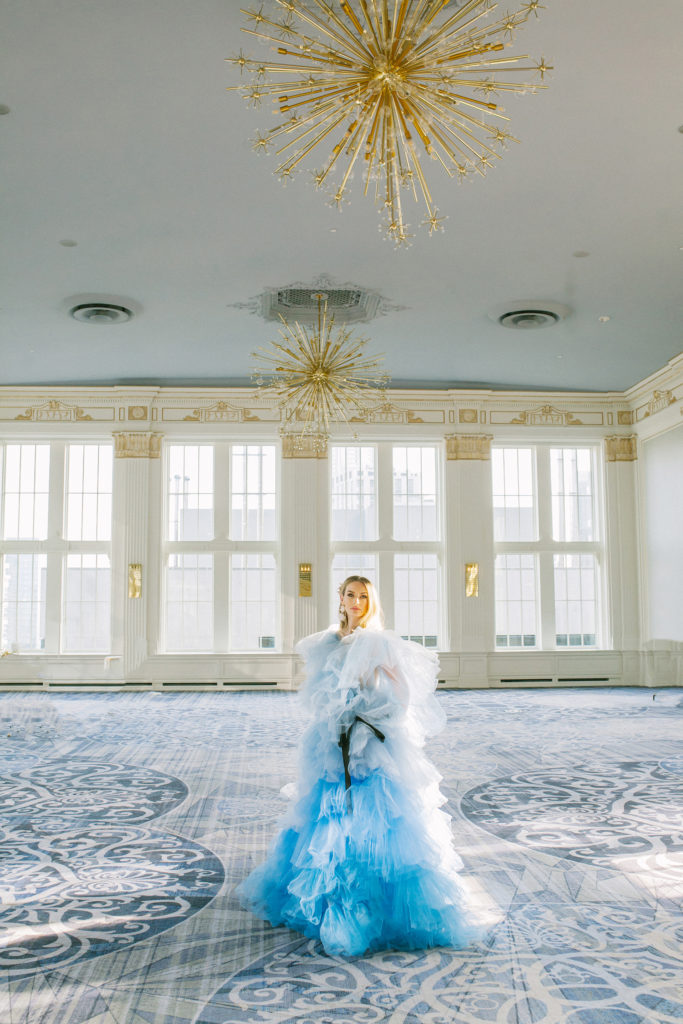 Bride in blue ruffle dress standing in ballroom with gold starburst chandeliers  | Weddings & Events by Cheryl Munro | Toronto Wedding Planner