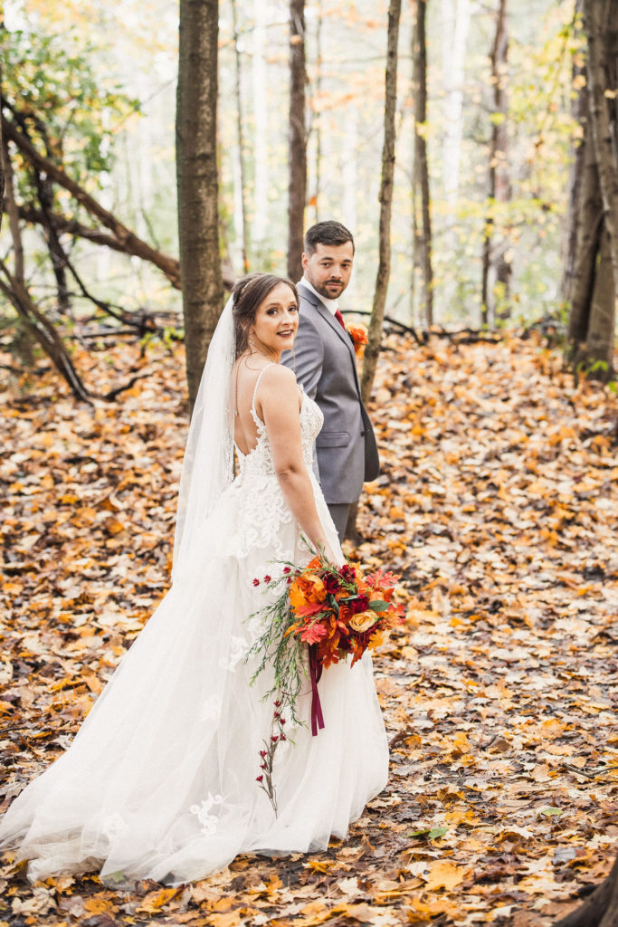 Bride and groom walking through a forest with fallen leaves | Weddings & Events by Cheryl Munro | Toronto Wedding Planner